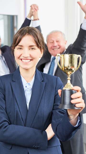 Uomini e donne in un ufficio, una con una coppa in mano, esultano per il conseguimento di un premio